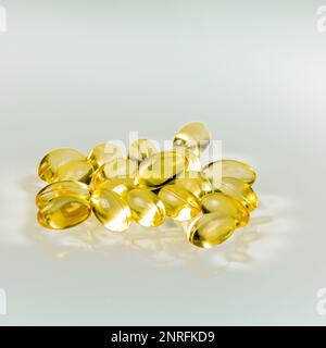 Pile de capsules de gel d'huile de poisson jaune réfléchie sur fond de verre. Banque D'Images