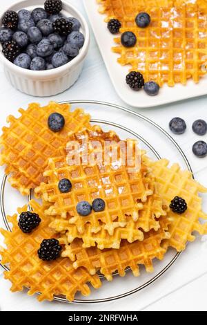 Gaufres sur la table et sur l'assiette. Bleuets et mûres dans un bol. Arrière-plan blanc. Banque D'Images