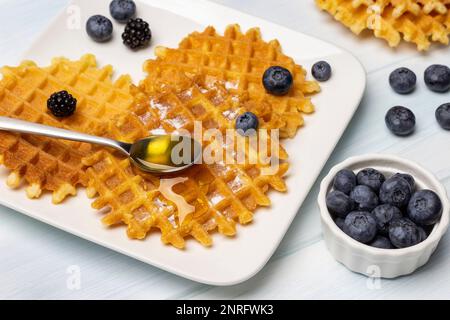 Bleuets dans un bol blanc. Cuillère de miel, gaufres et baies sur une assiette. Arrière-plan blanc. Banque D'Images