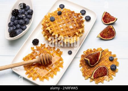 Un petit-déjeuner au miel et des gaufres sur une assiette blanche. Baies dans un bol. Figues et gaufres sur la table. Arrière-plan blanc. Banque D'Images