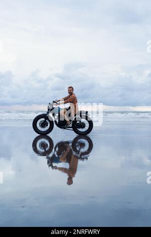 Un homme fait une moto le long de la plage au coucher du soleil. Banque D'Images