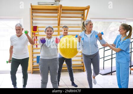 Physiothérapeutes aidant les femmes et les hommes âgés à faire de l'exercice en classe de forme physique Banque D'Images