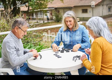 Groupe d'amis senior jouant des dominos sur la table dans le jardin de la maison de repos Banque D'Images