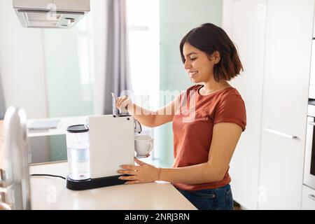 Souriante jeune femme arabe préparation du café avec machine dans la cuisine Banque D'Images