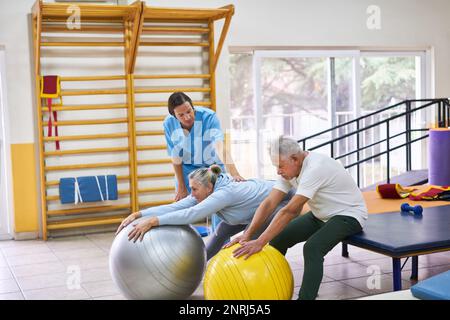 Femme et homme senior avec physiothérapeute guidant dans l'exercice sur les balles de fitness au centre de réadaptation Banque D'Images