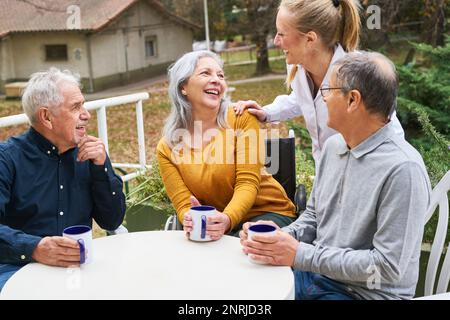 Infirmière parlant à un groupe heureux d'aînés dans le jardin de la maison de soins infirmiers Banque D'Images