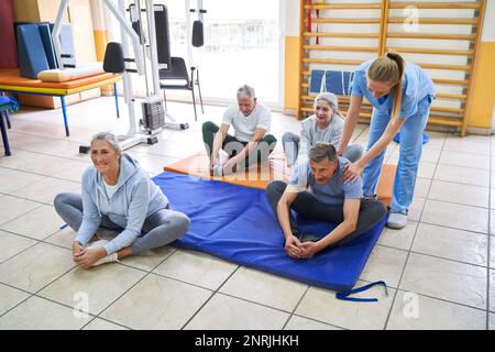 Femme instructeur personnes âgées pratiquant le cobbler poser en cours de fitness avec au centre de réadaptation Banque D'Images