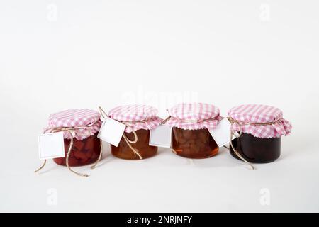 Un jeu de pots de confiture avec couvercles à carreaux roses et blancs et étiquettes vierges isolées sur un fond blanc Banque D'Images