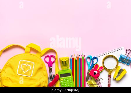 Retour à l'école, concept d'éducation Sac à dos jaune avec fournitures scolaires - bloc-notes, stylos, gomme arc-en-ciel isolé sur fond rose vue du dessus copie spac Banque D'Images