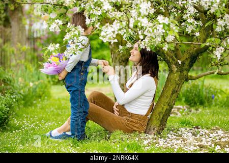 Jeune femme enceinte, la réception bouquet de fleurs colorées de son enfant pour la Fête des Mères, assis dans un beau jardin en fleurs de printemps Banque D'Images