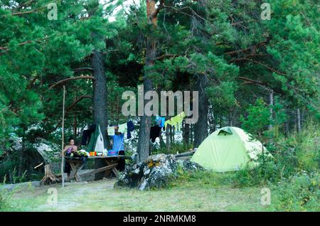 Une fille de touristes cuisiniers à une table à l'extérieur dans le parking près de la tente dans la forêt. Banque D'Images