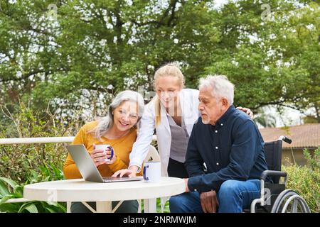 Une femme souriante discutant avec un couple âgé sur un ordinateur portable tout en prenant un café dans le jardin de la maison de retraite Banque D'Images