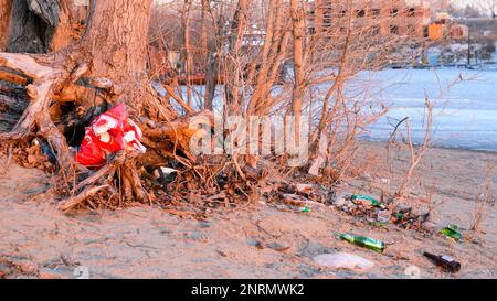 Une montagne de déchets avec un paquet de bouteilles en verre et en plastique se trouve sur la rive d'une rivière de la ville au printemps en Russie. Banque D'Images