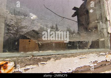 Lieu de résidence abandonné : fenêtre en verre recouverte d'épaisses toiles d'araignée, encadrée par un cadre en bois décadé. Banque D'Images