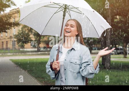 Jeune femme avec parapluie marchant sous la pluie dans le parc Banque D'Images