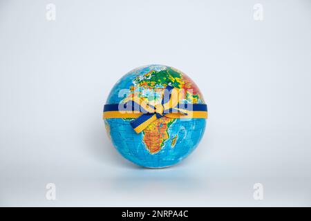 Globe attaché avec un ruban avec le drapeau de l'Ukraine sur un fond blanc gros plan Banque D'Images