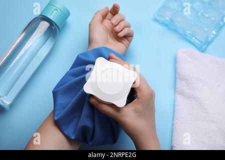 Femme avec compression à froid sur fond bleu clair, vue de dessus. Traitement par coup de chaleur Banque D'Images