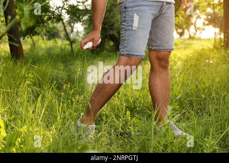 Homme appliquant un insectifuge sur la jambe dans le parc, gros plan. Prévention des piqûres de tiques Banque D'Images