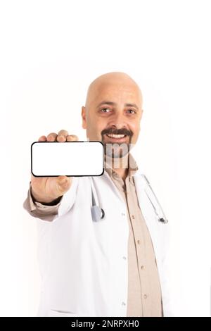 Portrait d'un médecin caucasien montrant un smartphone. Chauve, barbu homme beau tenant le téléphone mobile à l'horizontale. Écran blanc vierge pour maquette. Banque D'Images