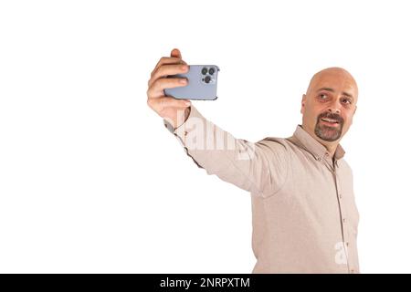 Portrait d'un homme millénaire caucasien prenant un selfie. Arrière-plan blanc isolé et debout. Tenir un smartphone moderne avec trois appareils photo. Un homme souriant. Banque D'Images