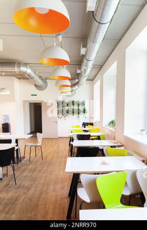 Lumière propre moderne loft minimalisme design école cafétéria avec de nombreux sièges vides verts ou bruns, des tables blanches et des lampes orange. Retour à l'école en bonne santé Banque D'Images