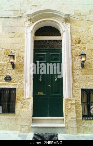 Porte traditionnelle de style classique en bois médiéval vert vintage peinte avec des knockers à la Valette, Malte. Mur en pierre jaune pastel avec lanternes. Banque D'Images