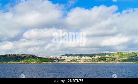Île Gozo, Malte. Printemps temps bleu ciel nuageux, herbe verte jeune et vue sur Mgarr et fort Chambray. Vue panoramique sur la mer. Arrière-plan horizontal long, Banque D'Images