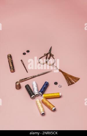 Encore la vie des kits de couture avec des bobines de fils de couleur, des articles et des ciseaux de cuivre vintage sur un fond rose Uni Banque D'Images