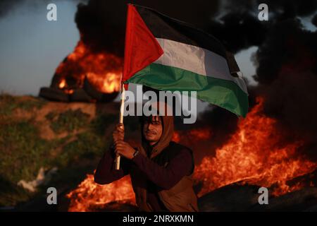 Les manifestants tiennent le drapeau palestinien devant des pneus en feu lors d'une manifestation le long de la frontière entre la bande de Gaza et Israël, en solidarité avec le camp de Jénine contre les opérations militaires israéliennes qui ont tué au moins neuf Palestiniens. Territoires palestiniens, Gaza. Banque D'Images