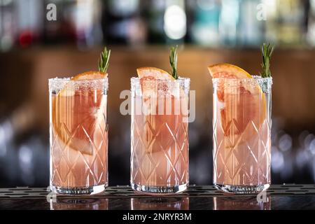 Trois cocktails paloma garnis de pamplemousse et de romarin placés sur le comptoir du bar. Banque D'Images