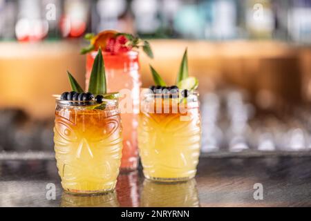 Cocktails mai tai dans des verres hawaïens garnis d'ananas, de bleuets et de fraises sur le comptoir du bar. Banque D'Images