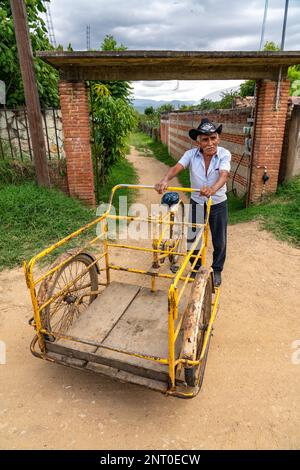 Un homme plus âgé dans un chapeau de cowbot avec son tricycle en face d'une porte de ferme à Santa Maria Coyotepec, Oaxaca, Mexique. Banque D'Images