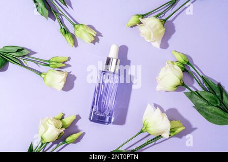 Bouteille cosmétique violette et fleurs d'eustoma blanches au soleil. Vue de dessus, plan d'agencement. Banque D'Images