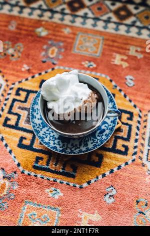 Chocolat chaud en bleu et blanc thé japonais et soucoupe recouverts de meringue assis sur un tapis orange Banque D'Images