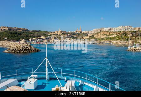 Le navire arrive au port de Mġarr sur l'île de Gozo, Malte. Belle ville sur les falaises et les collines en arrière-plan le jour ensoleillé du printemps. Banque D'Images