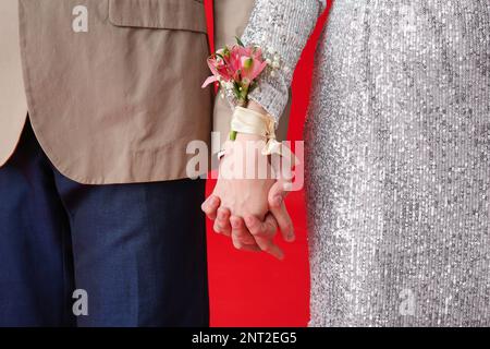 Jeune fille et sa date de bal tenant les mains sur fond rouge, gros plan Banque D'Images