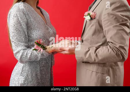 Jeune fille et sa date de bal tenant les mains sur fond rouge Banque D'Images
