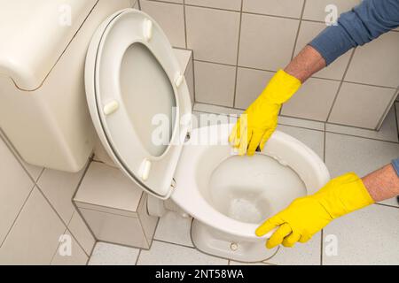 Mains d'un homme en gants jaunes nettoyant le bol des toilettes dans la salle de bains. Vue de dessus. Banque D'Images