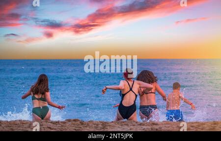Jeunes amis qui courent dans la mer au coucher du soleil à Bournemouth, Angleterre Banque D'Images