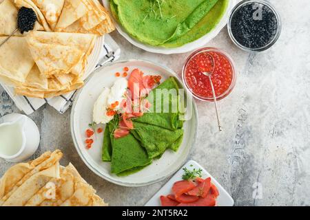 Assortiment de crêpes vertes et blanches. Fines crêpes d'épinards verts et de crêpe blanche avec caviar rouge et noir, sauce sur fond de table en béton gris Banque D'Images