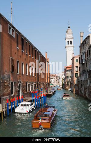 Bateaux-taxis et bateaux amarrés sur un canal étroit et bâtiments résidentiels de style architectural ancien, clocher de l'église penchée, San Marco, Venise, Italie. Banque D'Images