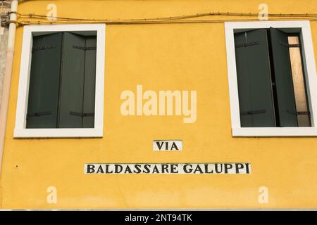 Via Baldassare Galuppi inscription sur le mur extérieur de la maison en stuc jaune avec des volets en bois vert, Piazza Baldassare Galuppi, Burano Island, Italie. Banque D'Images