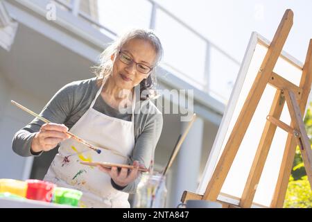 Bonne femme asiatique senior peignant sur un chevalet dans le jardin Banque D'Images