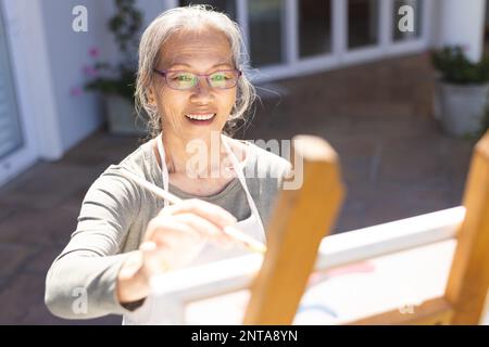 Bonne femme asiatique senior peignant sur un chevalet dans le jardin Banque D'Images