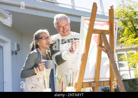 Heureux senior divers couple peinture sur chevalet dans le jardin Banque D'Images