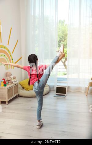 Jolie petite fille prenant cours de danse en ligne à la maison, vue arrière Banque D'Images