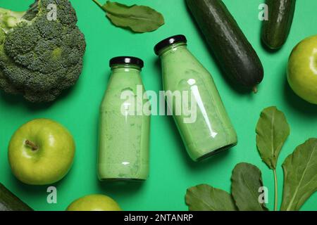 Bouteilles de délicieux smoothie et ingrédients sur fond vert, plat Banque D'Images