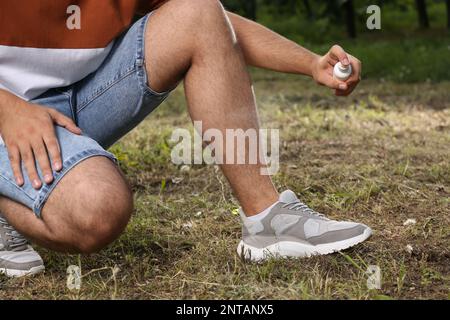 Homme appliquant un insectifuge sur la jambe dans le parc, gros plan. Prévention des piqûres de tiques Banque D'Images