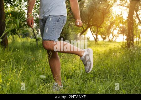 Homme appliquant un insectifuge sur la jambe dans le parc, gros plan. Prévention des piqûres de tiques Banque D'Images