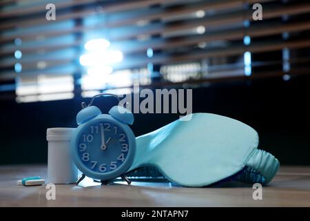 Réveil, masque de sommeil et pilules sur la table à l'intérieur. Traitement de l'insomnie Banque D'Images